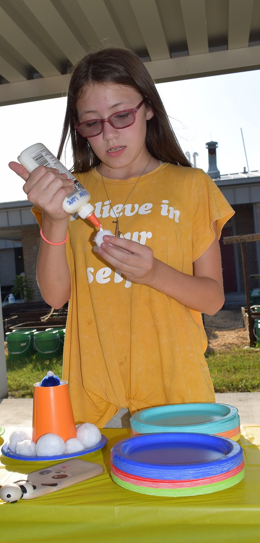 Fifth-grader Kylie Henrich puts glue on a white pom pom ball to stick on her sombrero, which was made with blue and white pom pom balls and an orange cup for the Florida Gators because she likes the team.