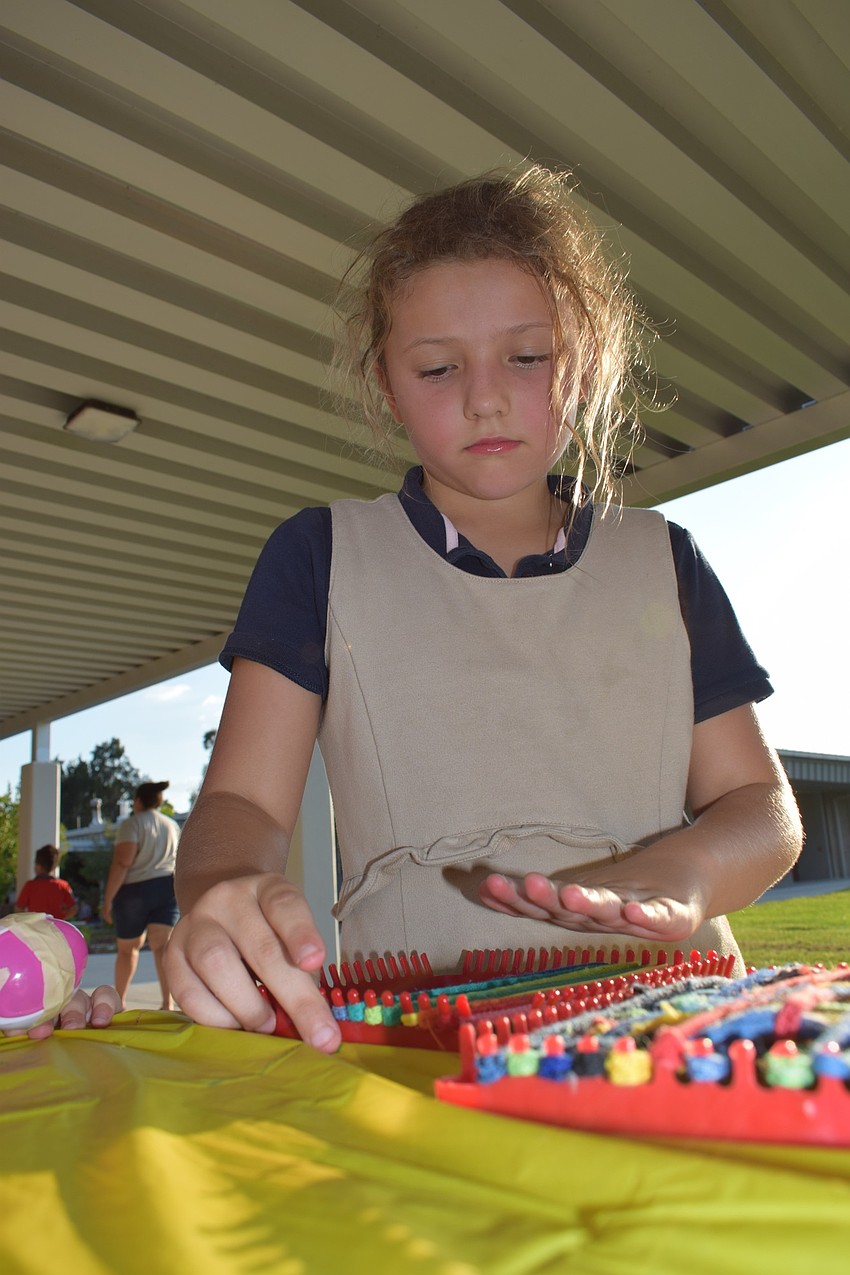 Third-grader Cayleigh Greer weaves bands in order of the rainbow on a small loom because rainbow is her favorite color.