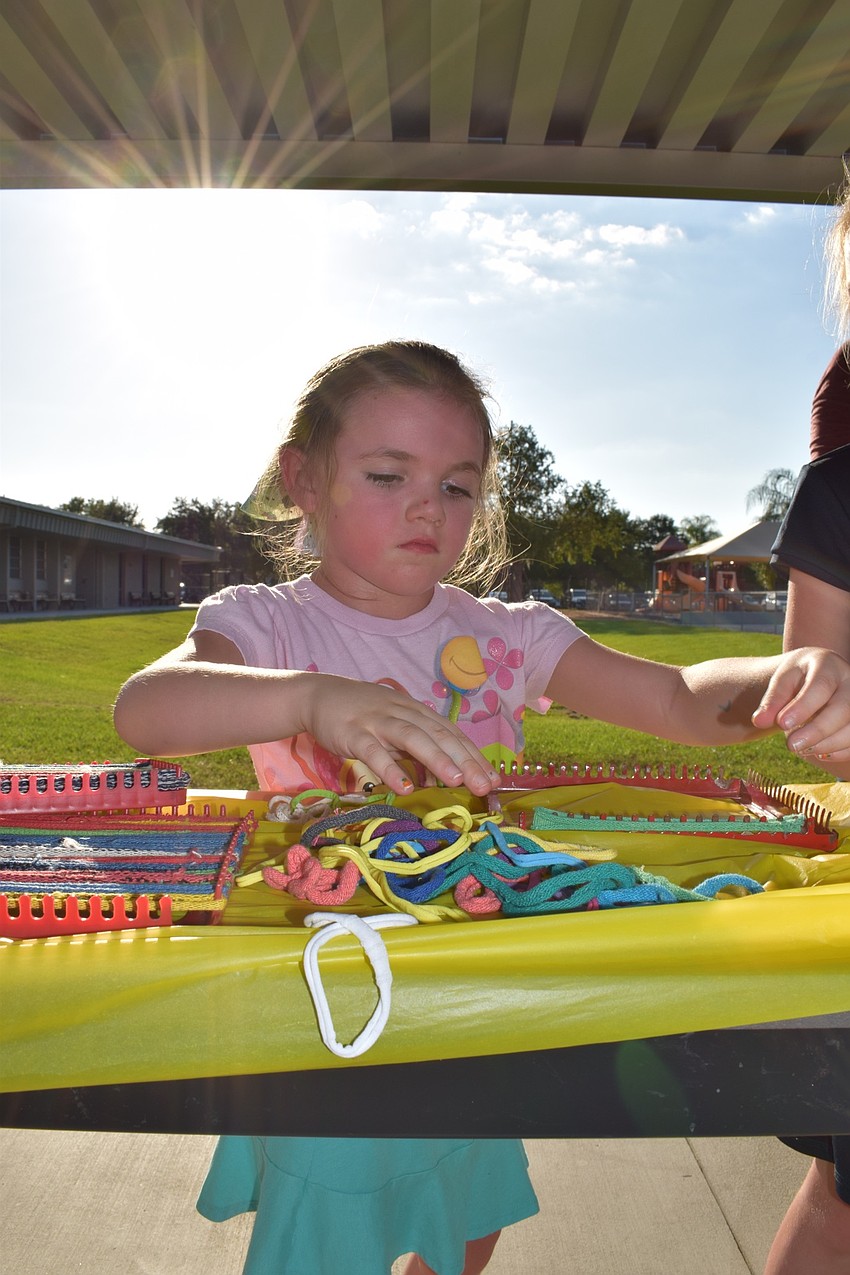 Pre-kindergartner Emery Ross, 4, weaves bands onto a small loom.
