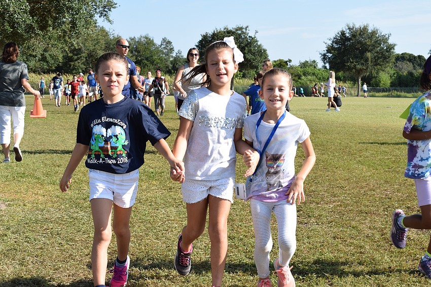 Second-graders Emma Horwath, Ava Wells and Bella Wells hold hands while running toward volunteers to mark the completion of a lap on their cards.