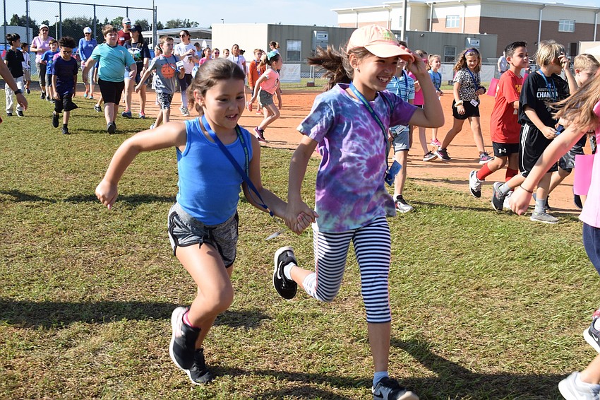 Third-grader Ava Sarid, holds hands with third-grader Erin Delong as they run to the start of the walk-a-thon.