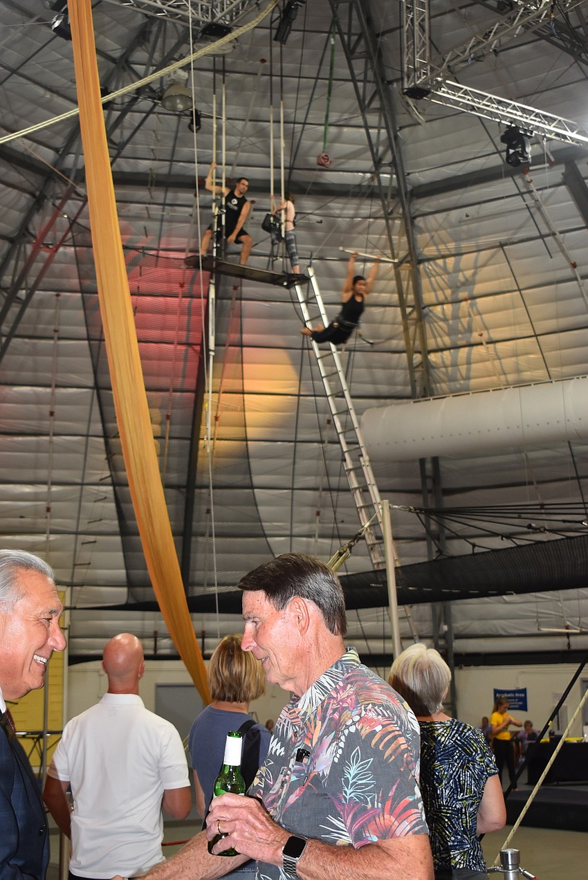 Attendees mingle as a trapeze artist takes flight.