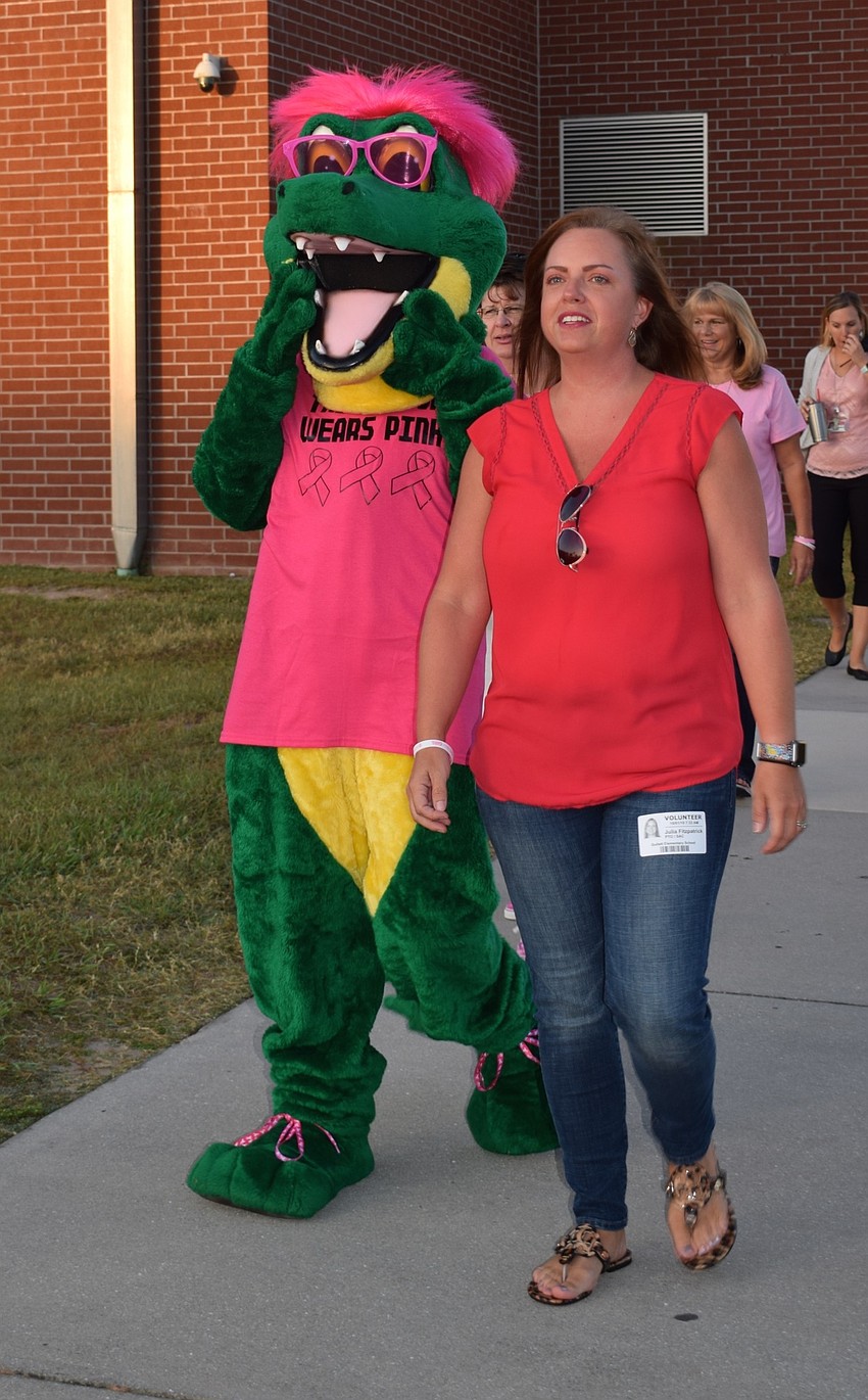 PTO member Julia Fitzpatrick walks outside with Chompy, B.D. Gullet Elementary School's mascot, decked out in pink before getting into the formation of a ribbon for an aerial photo.