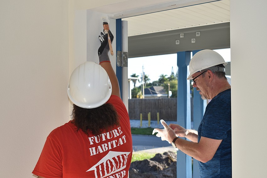 Robin Chacon paints above a door while Kenneth Blyth changes his gloves.