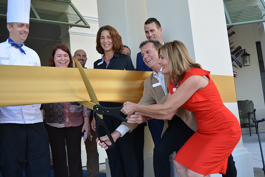 Grand Living at Lakewood Ranch Executive Director Michele Orlando, in red, and Grand Living  National Director of Sales and Marketing Bob Delle Donne (in front of ribbon) cut a ceremonial ribbon in front of staff members.