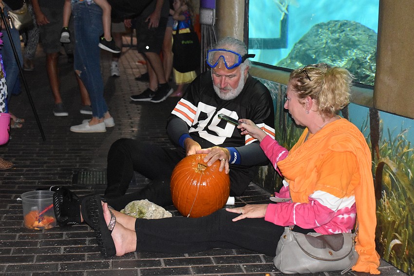 Mark Fishman carves a pumpkin after storms in the area kept him from carving it underwater while Terri Fishman holds a flashlight for him.