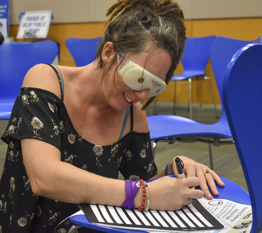 Tina Phillips learns to write with vision impairment glasses on.