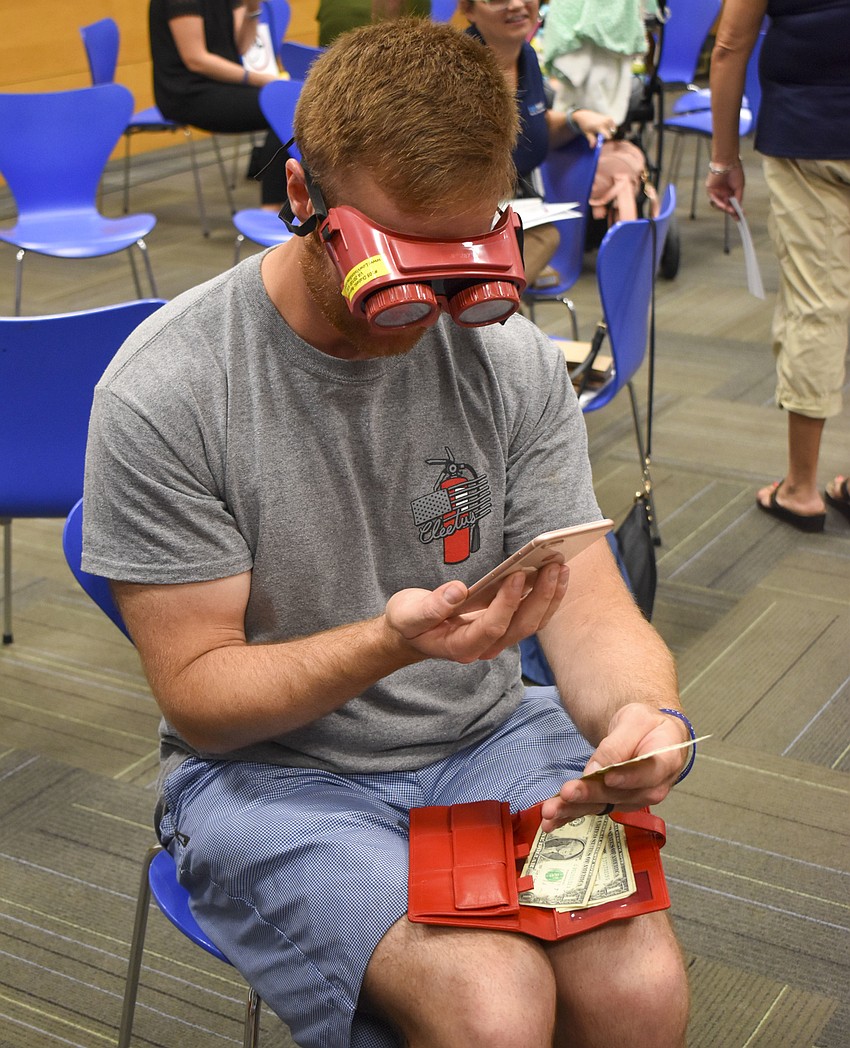 Dan Spencers tries to find $1.75 from a wallet while wearing vision impairment goggles.