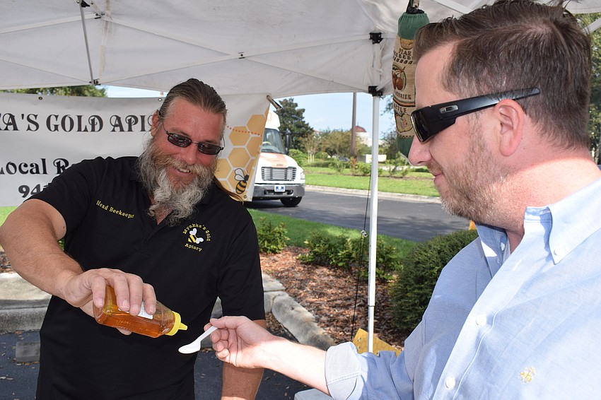 Myakka's Gold Apiary owner Jim Cutway gives Lakewood Ranch's Jayson Quinn a taste of his honey at the opening day of the Market at Lakewood Ranch.