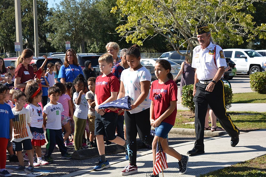 Caden Parker, Gianna Gonzalez and Lily Asher present the American flag with Navy veteran and VFW Post 12055 member Graham Ellis, behind.