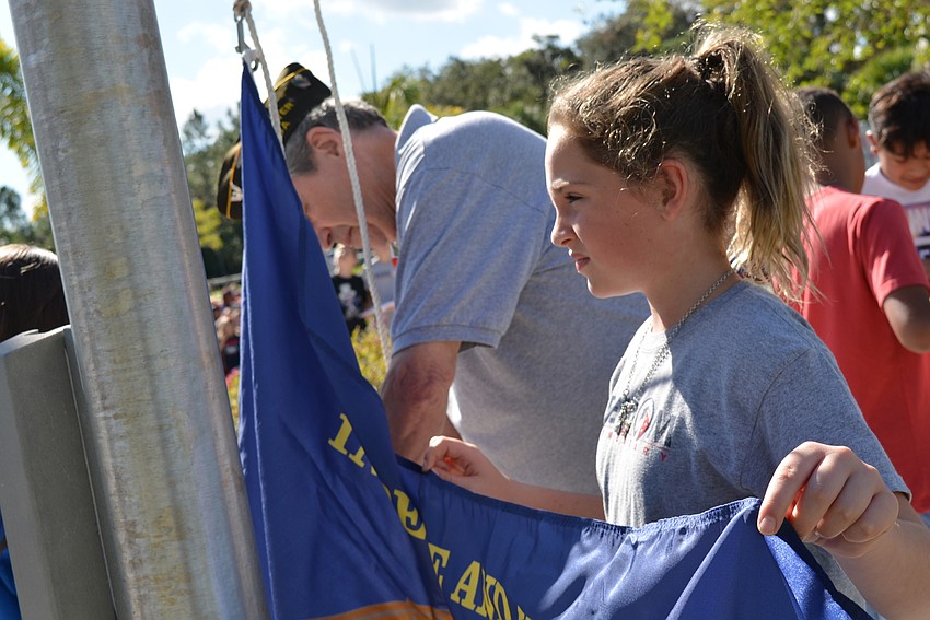 Fourth-grader Rebecca Creel  helps VFW Post 12055 veteran Ernie Friedman raise a military flag during the courtyard ceremony.