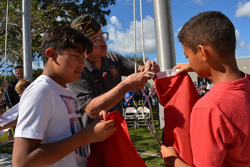Fifth-graders Gerardo Ponce and Landon McFarland help VFW Post 12055 member Ron Leonard raise the flag for the U.S. Marines.