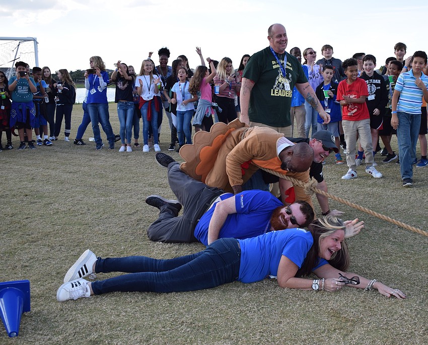 Teachers and staff members stumble and fall to the ground leaving the eighth graders victorious in a tug of war.
