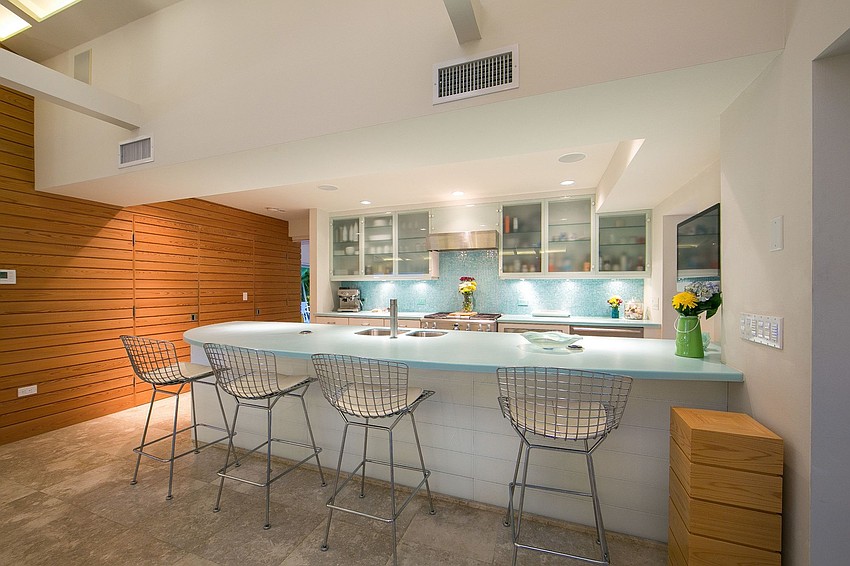 he sleek kitchen is crafted with blue glass mosaic tile backsplash, custom white cabinetry accented with glass, and world-class stainless-steel appliances.