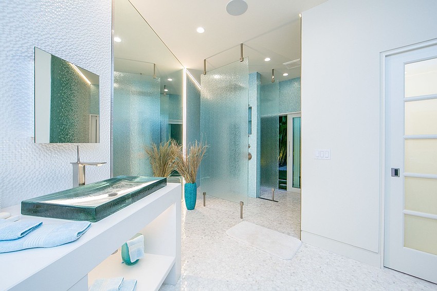 he sleek kitchen is crafted with blue glass mosaic tile backsplash, custom white cabinetry accented with glass, and world-class stainless-steel appliances.