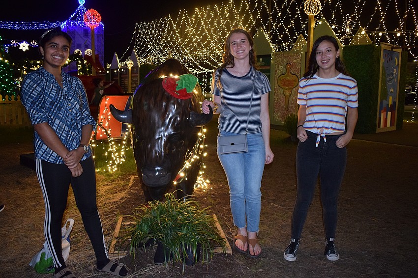 Mrinalini Rajeev, of Sarasota, Julia Kourelakos, of Palma Ranch, and Allyson Weissert, of North Port, take a photo in front of a buffalo decorated with lights. Rajeev said the lights around the lake were cool.