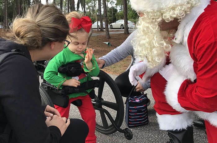 Longboat Key Fire Chief Paul Dezzi, dressed as Santa Claus, stoops down to greet 3-year-old Lili Michel on Dec. 21 at Nathan Benderson Park as Lili's mother, Katrina (left), watches. (Photo courtesy of Longboat Fire Department)