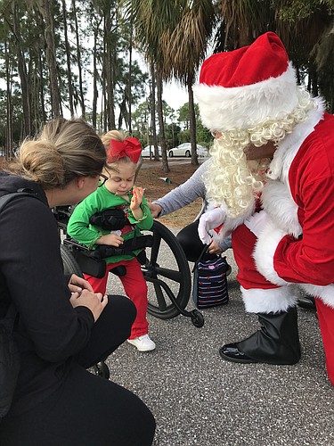 Longboat Key Fire Chief Paul Dezzi, dressed as Santa Claus, stoops down to greet 3-year-old Lili Michel on Dec. 21 at Nathan Benderson Park as Lili&#39;s mother, Katrina (left), watches. (Photo courtesy of Longboat Fire Department)