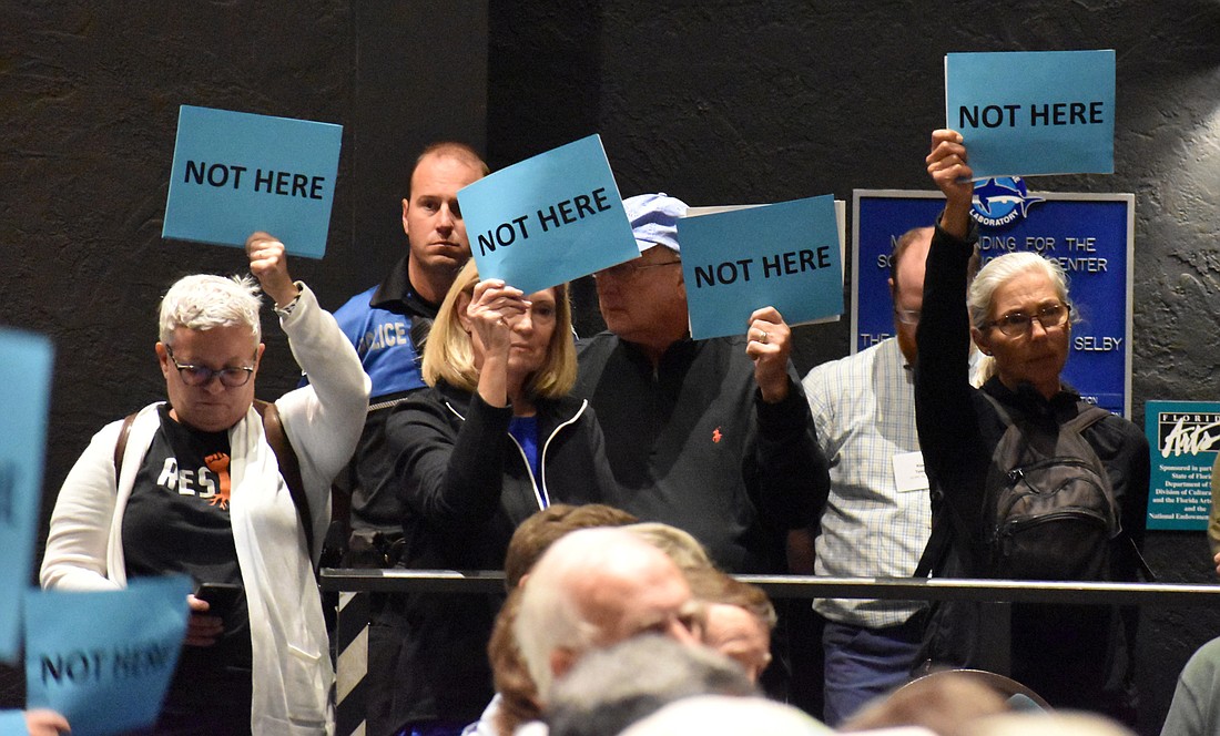 Residents hold up "No Fish Farm" and "Not here" signs as supporters of the project speak.