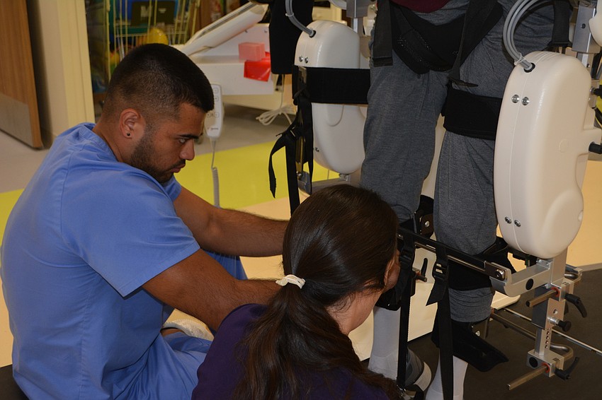 Physical therapist Dr. Julia Figueroa (center) and rehab tech Daniel Gonzalez (left) adjust the Hocoma Lokomat to stroke patient Ronald Serres's legs. The Lokomat controls the amount of weight Serres feels on both sides.
