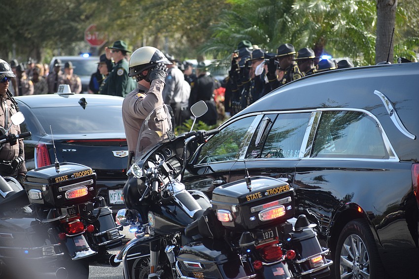 A law enforcement officer salutes the hearse carrying the casket of Trooper Joseph Bullock.