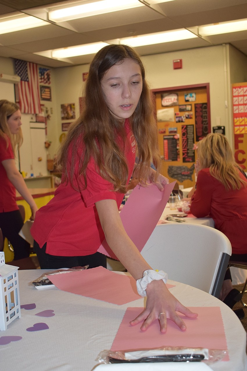 Liliana Vazquez, an eighth grader and president of the Family Career and Community Leaders of America, puts new place settings on the table for new guests. 