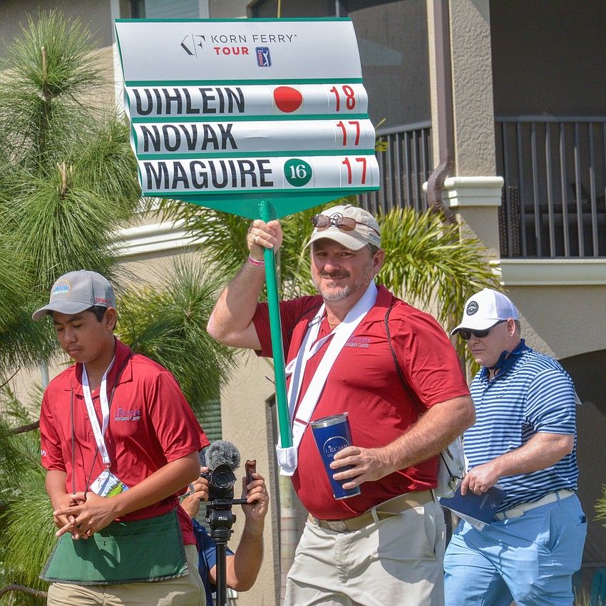 Volunteer Bryan Veith carries the leaderboard for the group of Andrew Novak, Peter Uihlein and Jack Maguire.