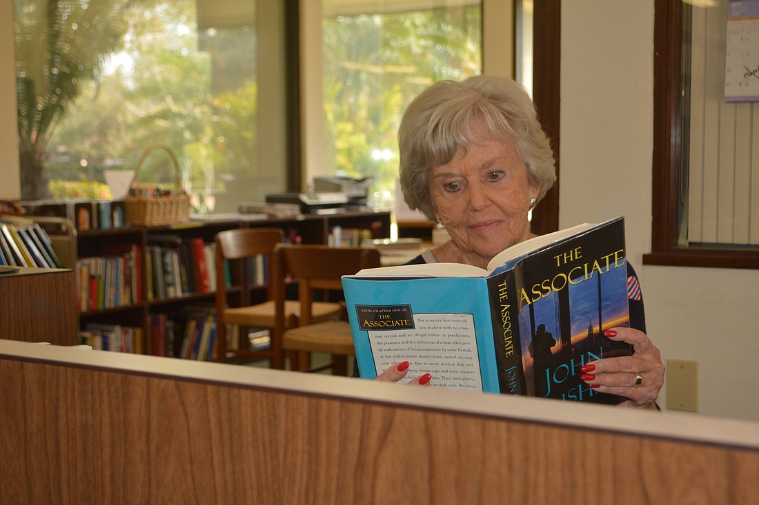 Longboat Library volunteer librarian Bonney Libman reads "The Associate" by John Grisham during her shift Friday.