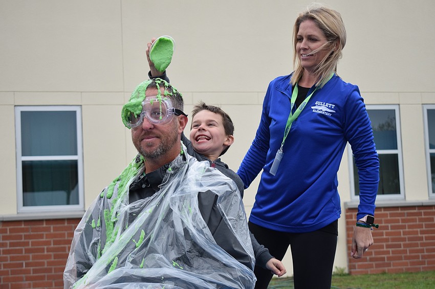 Principal Todd Richardson sits quietly while kindergartner Ethan Decker pours slime on his head and Kristin Pomeroy, Parent-Teacher Organization president, watches. 