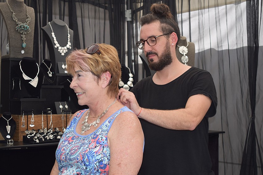 Bradenton resident Susan Woods stands still while artist Emre Tekeli puts on a one-of-a-kind necklace on her. 