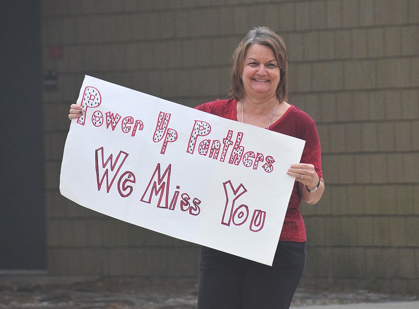 Jill Bergeron, family and consumer science teacher at Braden River Middle School, holds up a hand-made sign as families pick up devices for online learning. 
