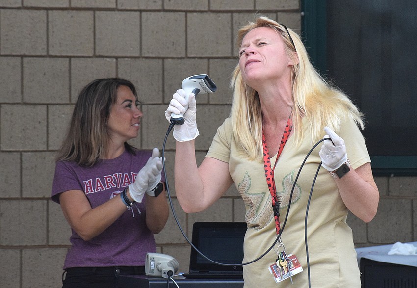 Analia Mansi, a bookkeeper at Braden River Middle School, claps along as Assistant Principal Kristen Cunningham sings along to a song using a scanner as a microphone.