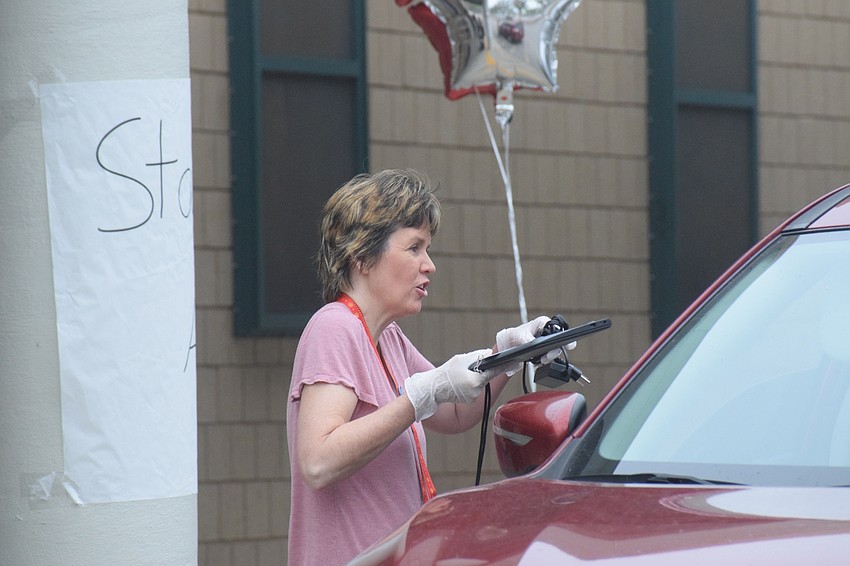 Lisa Dudas, a paraprofessional at Braden River Middle School, hands a family a device for students to use during online learning.