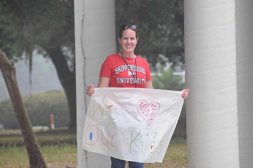 Jennifer Hall, a science teacher at Braden River Middle School, holds a sign up as families drive by.