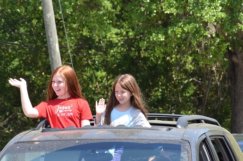Molly and Maggie Neary stand through the sun roof of their car to greet teachers at Braden River Elementary School.