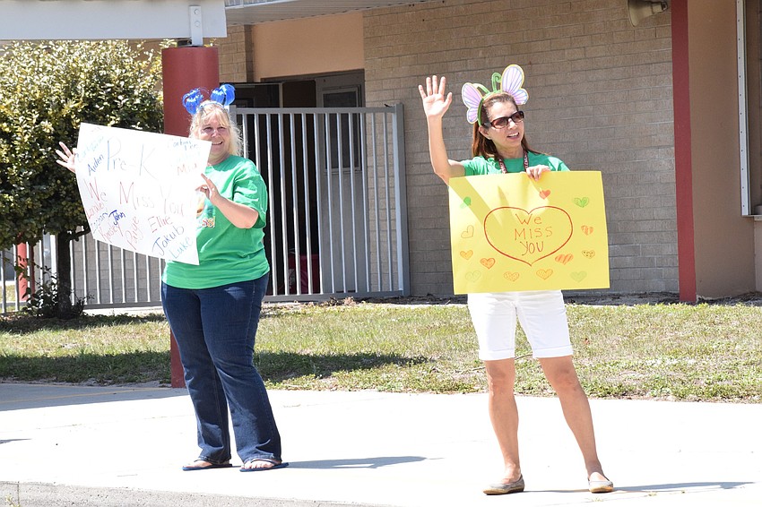 Jodi McCoy, a pre-kindergarten teacher at Braden River Elementary School, and Claudia Greene, a teacher aid, wave to students as they come by in their cars.