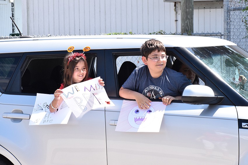 Ava and Jack Phillips make and hold signs for their teachers as they drive by the student pick-up loop of the school.