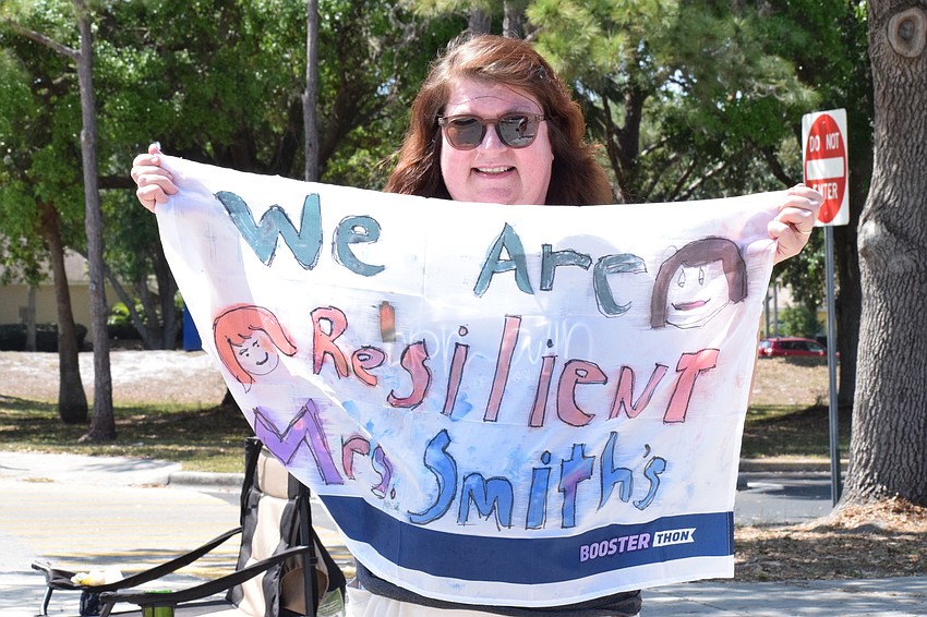 Pamela Smith, a second grade teacher, carries a flag with her class' motto, 'We are resilient,' on it as they drive by.