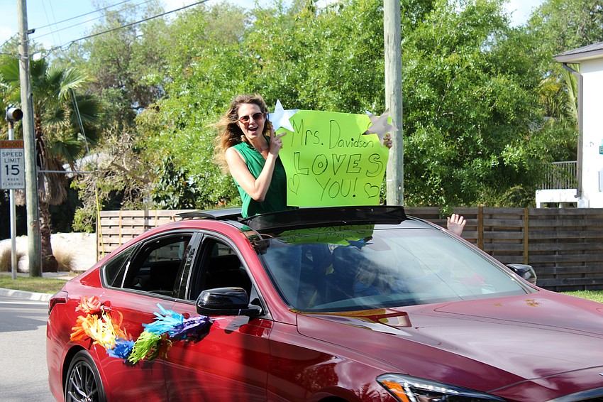 Teachers hold up signs with messages for their students.