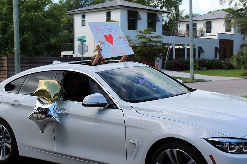 Teachers hold up signs with messages for their students.