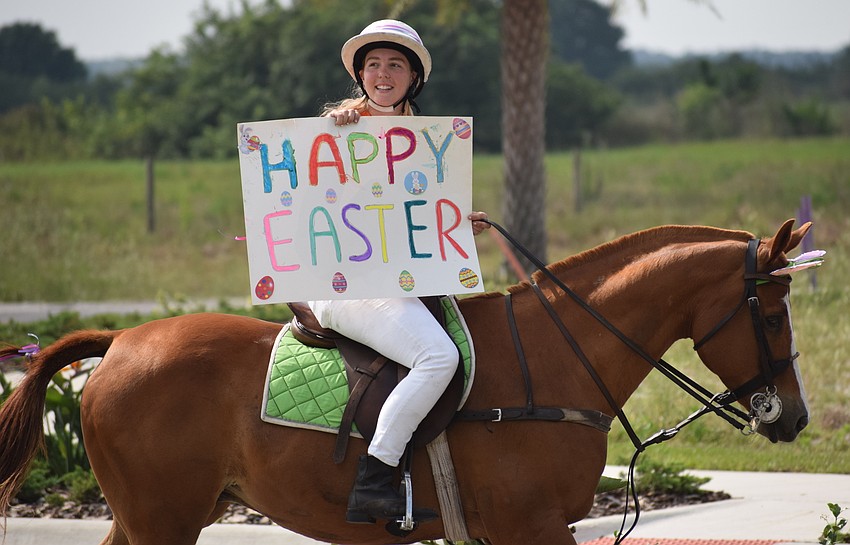The Sarasota Polo Ranch's Pippa Campbell shows the message as she rides in a makeshift Easter parade put together to entertain the residents at Grand Living at Lakewood Ranch.