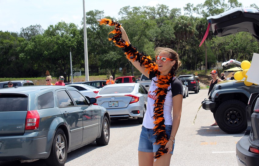 Debbie Kaplan waves a feather boa as students drive by.
