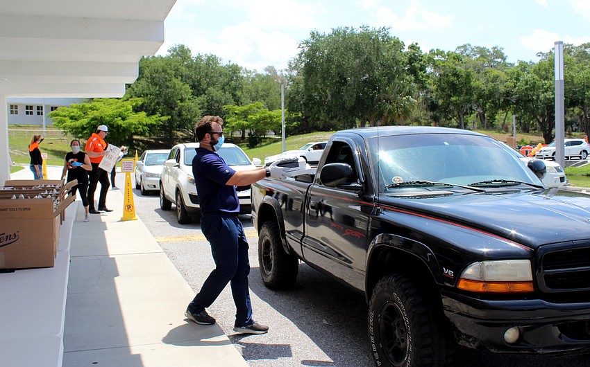 Teachers hand students their caps and gowns through their car windows.