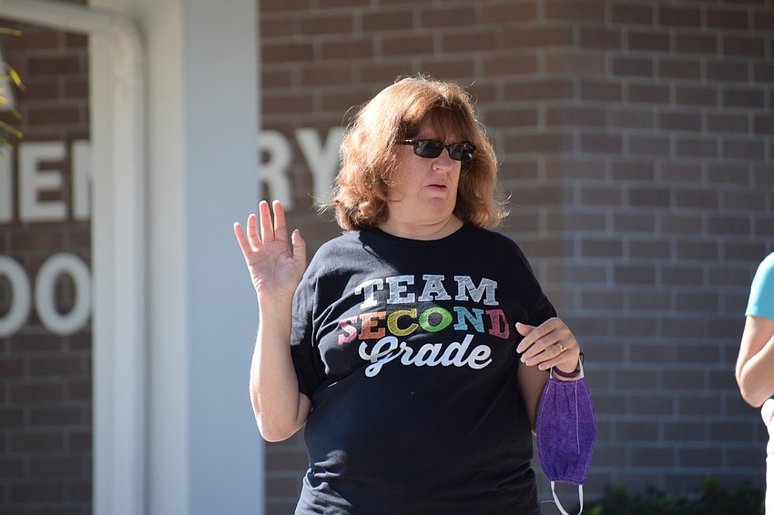 Luci McGee, a second grade teacher at Tara Elementary School, waves to students passing by in their cars.