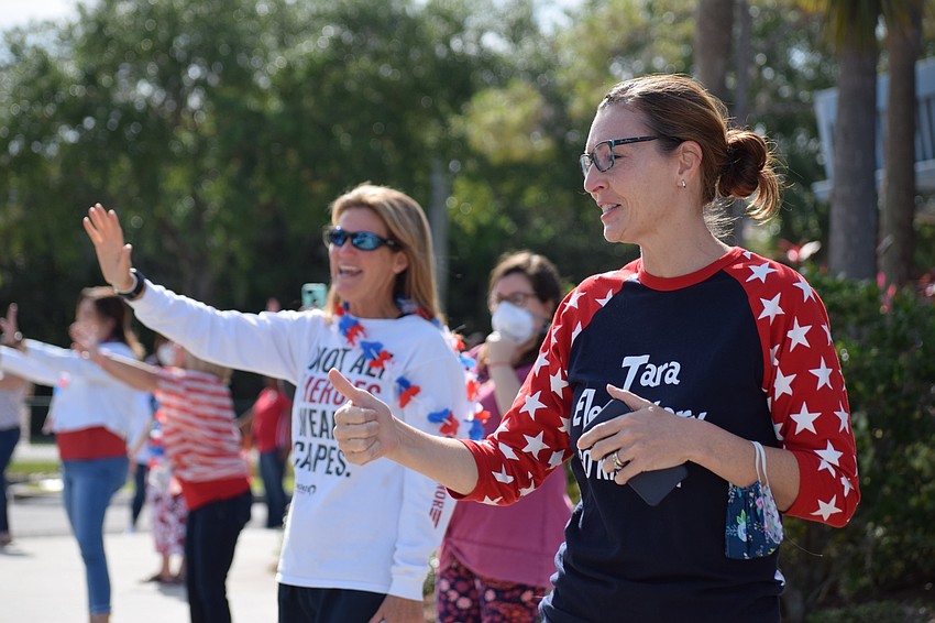 Amy Teta, a physical education teacher at Tara Elementary School, and Laura Campbell, principal of Tara, wave to students as they go by in their cars.