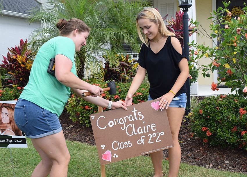 Hannah Kessie, a youth pastor at Oasis Church, helps put up a yard sign congratulating Clair Sidnam, a senior at Lakewood Ranch High School. Sidnam was supposed to graduate May 13, but the ceremony was postponed until July.
