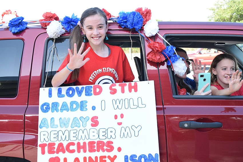 Lainey Ison, a fifth grader at Freedom Elementary, shows the sign she made while waving to teachers and staff members.