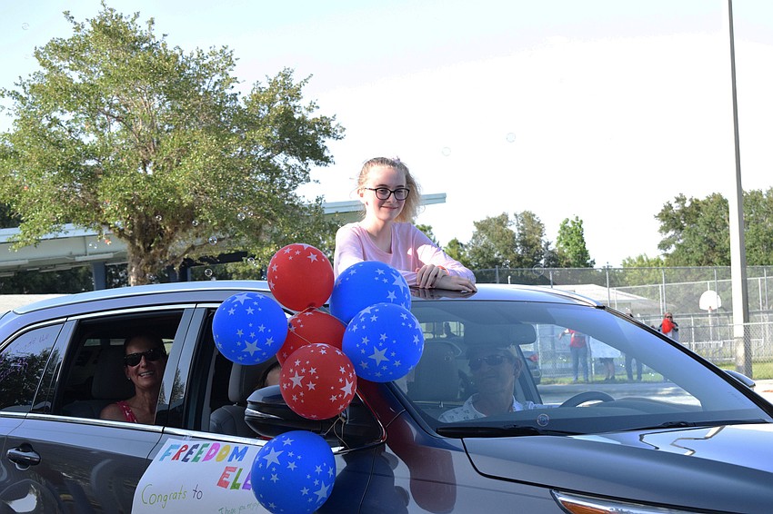 Elizabeth Pierce, a Freedom Elementary fifth grader, stands out of her car's sun roof to wave to teachers and staff.