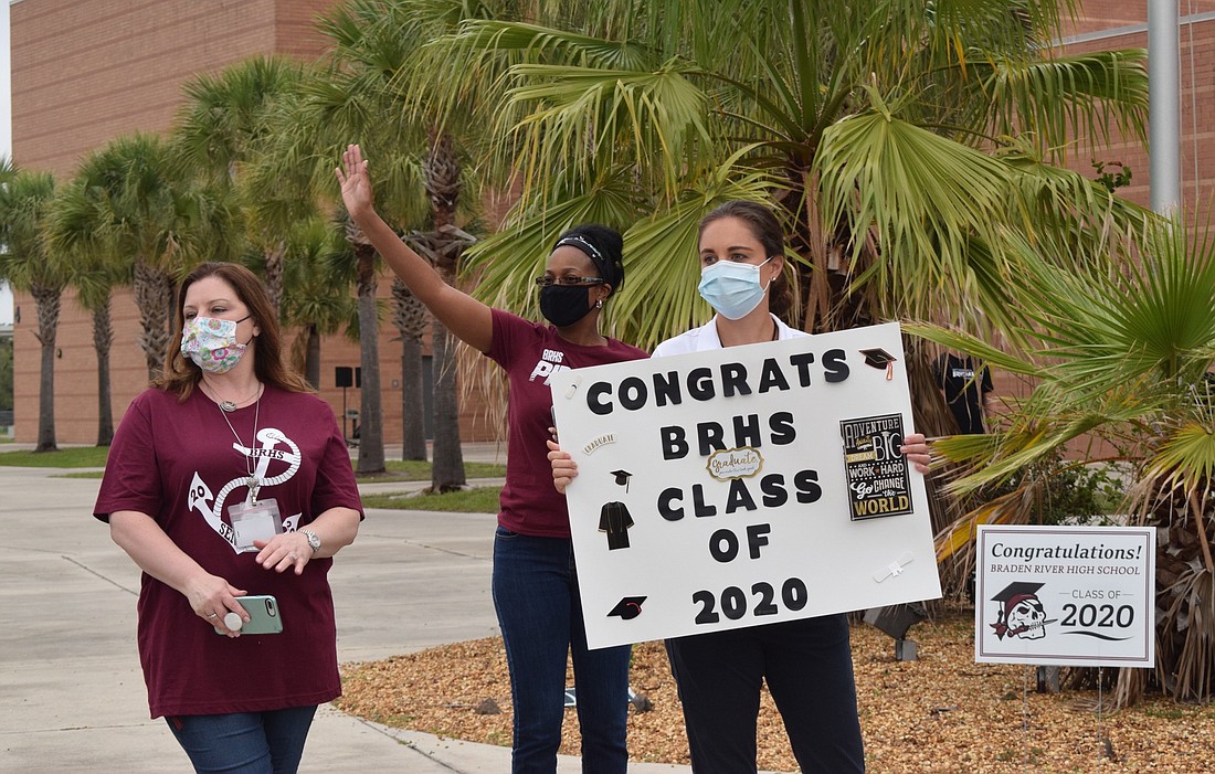 Braden River High School nurse Dayna Grella, receptionist Avis Boldin and school counselor Kirsten Lawlor wave and cheer for seniors as they drive by to pick up their caps and gowns.