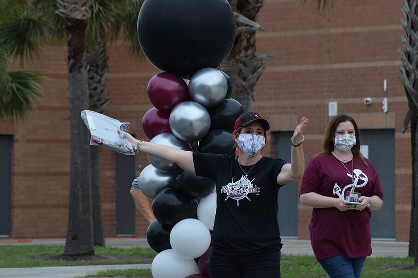 Kymmie Marriner, a social studies teacher and senior advisor, holds out a cap and gown for a senior while Dayna Grella, a school nurse, cheers.
